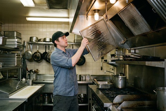 Worker lifting a mesh baffle filter out of a commercial range hood