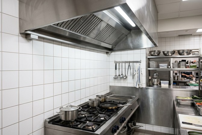 Bright stainless steel exhaust hood over a white tiled kitchen wall